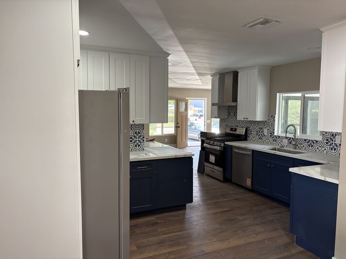 Remodeled kitchen with navy lower cabinets, white uppers, and patterned blue tile backsplash