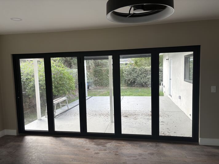 View through open accordion doors to patio, lawn, and landscaped yard